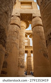 A dramatic vertical shot inside the Great Hypostyle Hall at Karnak Temple in Luxor, Egypt, with towering columns leading the eye upward toward the ancient clerestory stone grille windows that once filtered light into the hall. Tiny figures of visitors at the base emphasize the extraordinary height of the structure, one of ancient Egypt greatest architectural achievements.