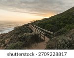 Dramatic vertical sunset view over the wild coastline of Robberg Nature Reserve, Plettenberg Bay, South Africa. The golden hour casts a vibrant orange glow over the crashing waves and rocky shoreline.