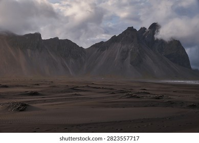 Dramatic Vestrahorn mountain range towering over vast black sand dunes under moody cloudy sky at Stokksnes - Iceland