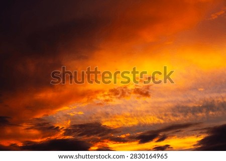 A dramatic and vibrant sunset sky filled with fiery orange clouds and dark silhouettes, creating a breathtaking and cinematic natural landscape background.
