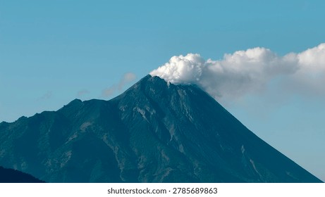 Dramatic view of an active volcano mountain emitting smoke under a clear blue sky. Perfect for travel, nature, geology, adventure, disaster, environmental, and landscape-themed projects, backgrounds, blogs, documentaries, and editorial content.