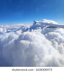Dramatic view of an airplane wing piercing through fluffy white cumulus clouds against a vast deep-blue sky, evoking freedom, wonder and limitless horizons.