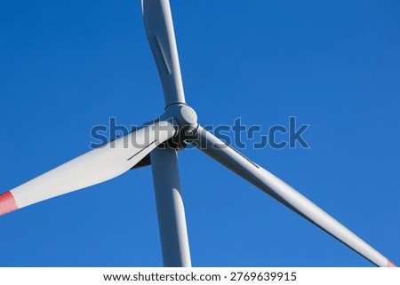 A dramatic view from below captures the rotor and blades of a wind turbine against a vivid blue sky.