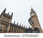 Dramatic view of Big Ben and the Gothic Houses of Parliament with an ornate street lamp in London, UK.