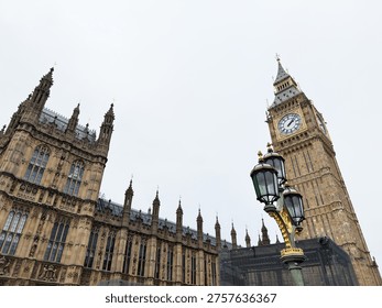 Dramatic view of Big Ben and the Gothic Houses of Parliament with an ornate street lamp in London, UK.