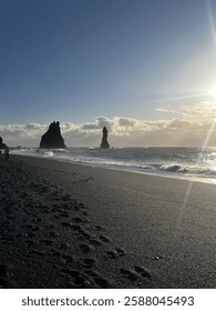 A dramatic view of Iceland’s Black Sand Beach, where powerful waves crash against the dark volcanic shoreline. Towering sea stacks rise in the distance, framed by moody skies and rugged coastal beauty