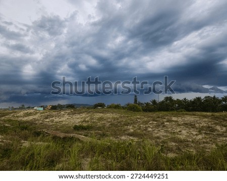 A dramatic view of a cloudy sky over a tranquil beach, with dark, menacing clouds approaching the horizon, surrounded by lush vegetation.