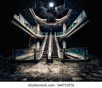 Dramatic view of damaged escalators in abandoned building. Full moon shining on cloudy night sky through collapsed roof. Apocalyptic and evil concept