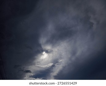 A dramatic view of a dark cloudy sky with the sun peeking through the clouds.