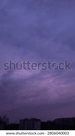 A dramatic view of dark purple clouds filling the evening sky above city buildings.