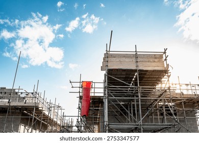 Dramatic view of early evening scaffolding seen on a new housing development in the UK. The sun is seen setting behind some of the scaffolding poles.