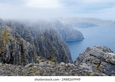 A dramatic view from the edge of a cliff, looking out over the vast, blue ocean shrouded in mist. Nordkapp, North Cape Norway - Powered by Shutterstock