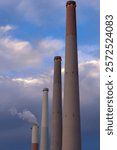 Dramatic view of four ascending industrial chimneys at Orot Rabin power station in Hadera, Israel, captured against a moody blue sky with white clouds during golden hour