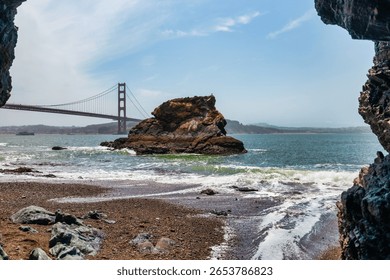 Dramatic view of the Golden Gate Bridge from a rocky cave at Kirby Cove Beach, San Francisco. Ocean waves, rugged cliffs, and vivid colors create a cinematic coastal scene ideal for travel and nature