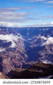 Dramatic view of the Grand Canyon with deep canyon walls and low clouds floating between the cliffs.