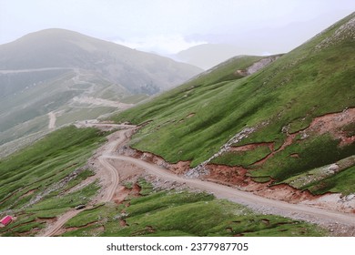 Dramatic view of green hill with marks of landslide everywhere and dirt road.