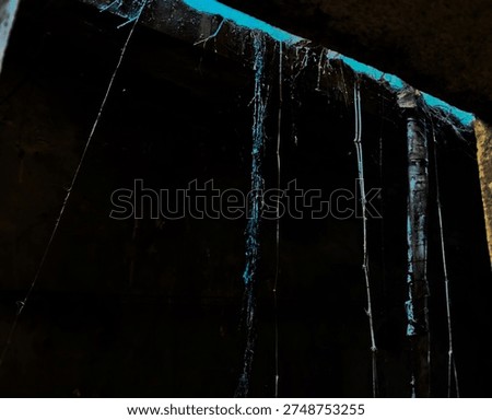 Dramatic view of hanging roots and debris illuminated by a bright turquoiseblue light source from a narrow opening in a dark, mysterious underground passage or cavern.