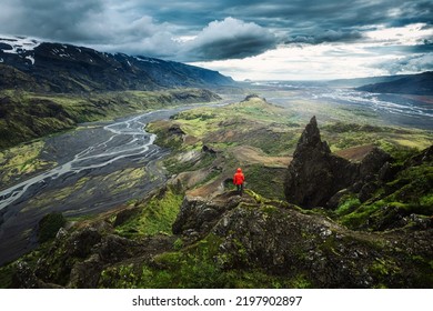 Dramatic view of Hiker man in red jacket standing on top of Valahnukur viewpoint surrounded by volcanic mountain and Krossa river in Icelandic Highlands at Thorsmork, Iceland