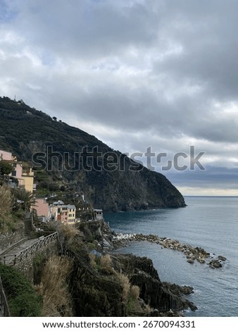 A dramatic view of the hiking trail and a historic village on the rugged cliffs of Cinque Terre, Italy. A moody and atmospheric coastal landscape on an overcast day.