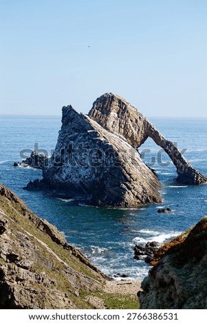 Dramatic view of the iconic Bow Fiddle Rock, a natural sea arch located on the Moray coast near Portknockie, Scotland, under a clear blue sky.
