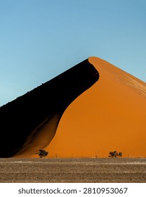 A dramatic view of an immense ochre sand dune set against a striking blue sky in Sossusvlei, Namib Desert
