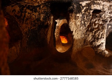 Dramatic view inside Derinkuyu Underground City, Cappadocia, Turkey. Warm golden light illuminates hand-carved volcanic tuff tunnels and arched doorways, evoking ancient refuge for Hittites, Phrygians, Byzantines, Umayyads, and early Christians. UNESCO World Heritage marvel ideal for travel campaigns, history books, archaeology docs, adventure posters, mystery films.