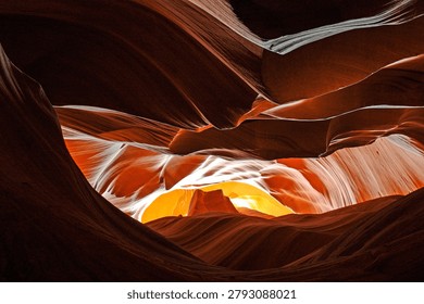 A dramatic view inside a red sandstone slot canyon with layered curved rock walls, deep shadows, and bright sunlight illuminating warm orange formations.