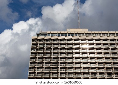 Dramatic view of a large building glistening in the sunlight, with dramatic cloudy sky behind.