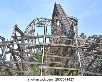 Dramatic view of a large wooden roller coaster with intricate support beams and towering tracks against a blue sky. Captures engineering, entertainment, thrill rides, tourism, and amusement park attractions.