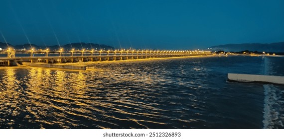 A dramatic view of a lighting bridge arching over serene waters, illuminated by vibrant hues. The reflection on the water creates a mesmerizing, colorful display, blending modern engineering with natu