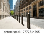Dramatic view of a line of security bollards located outside a central London government building in Pimlico. A single person can be seen walking g down the pavement to the glass office block.