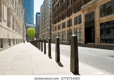 Dramatic view of a line of security bollards located outside a central London government building in Pimlico. A single person can be seen walking g down the pavement to the glass office block.
