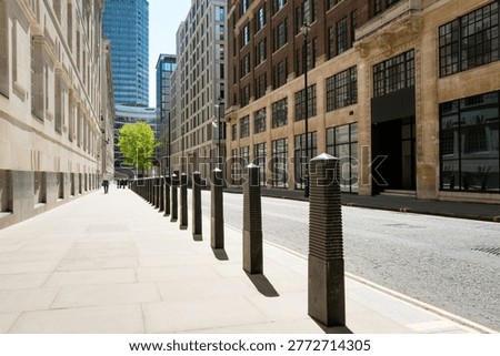Dramatic view of a line of security bollards located outside a central London government building in Pimlico. A single person can be seen walking g down the pavement to the glass office block.