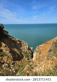 Dramatic view looking down a rocky white chalk cliff ravine to the turquoise ocean in Etretat, Normandy, France for travel, tourism, and coastal nature background copy space.