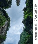 Dramatic view looking up at lush green limestone cliffs and cloudy sky