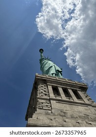 A dramatic view looking up at the Statue of Liberty from the base, capturing the iconic arm holding the torch and the points of her crown. This perspective highlights the monument's architectural deta