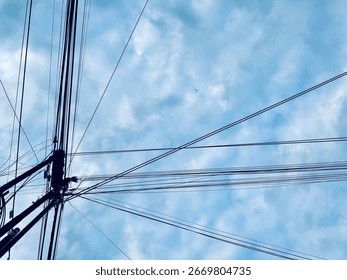 A dramatic view looking up at a utility pole with a complex network of power and communication lines stretching outward, silhouetted against a cloudy blue sky, symbolizing urban connectivity.