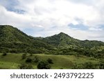 Dramatic view of lush green hills stretching wide under gray cloudy skies. Dark clouds gathered on the horizon, creating a mysterious and serene atmosphere.