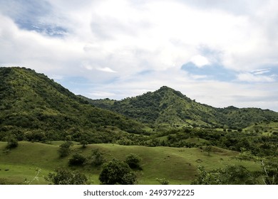 Dramatic view of lush green hills stretching wide under gray cloudy skies. Dark clouds gathered on the horizon, creating a mysterious and serene atmosphere. - Powered by Shutterstock