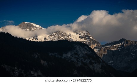 Dramatic view of mountain peaks covered with snow and shrouded in white clouds at sunset, Swiss Alps.