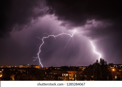 A dramatic view of a nighttime thunderstorm with bright lightning bolts cutting through the dark sky over the city. 