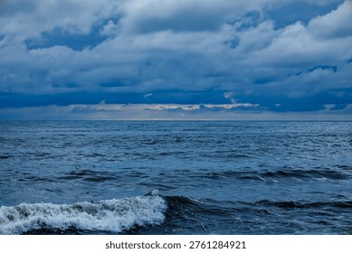 Dramatic view of ocean waves crashing against the shore under a heavy, dark cloudy sky, suggesting an approaching storm or rainy weather.