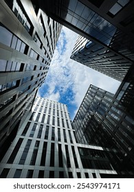 Dramatic view of office skyscrapers with reflections against a cloudy sky, shot from below.