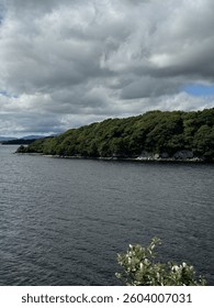 Dramatic view over a calm lake with dense forest shoreline and moody clouds drifting across the sky.