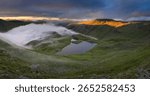 Dramatic view overlooking Sprinkling Tarn with golden light on mountains in The Lake District, UK.