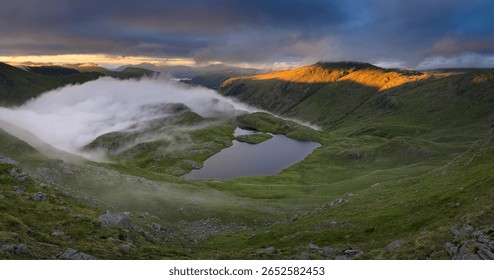 Dramatic view overlooking Sprinkling Tarn with golden light on mountains in The Lake District, UK.