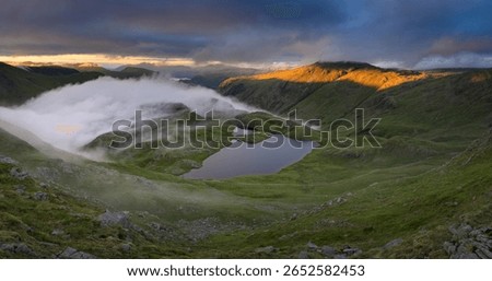Dramatic view overlooking Sprinkling Tarn with golden light on mountains in The Lake District, UK.