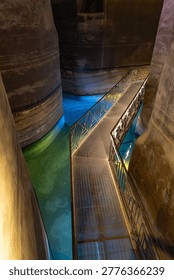 A dramatic view of the Palombaro Lungo, a massive 19th-century water cistern carved into the calcarenite rock beneath Piazza Vittorio Veneto, showcasing its cathedral-like proportions and glowing blue-green water