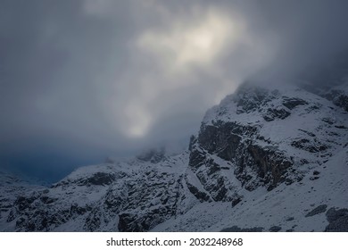 Dramatic view of Kościelec Peak, High Tatra Mountains, Poland. Sunlight behind the clouds covering the summits. Selective focus on the rocks, blurred background.