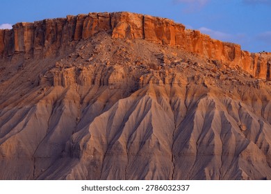 A dramatic view of a reddish-orange sandstone cliff contrasting with eroded gray soil structures under a clear blue sky.